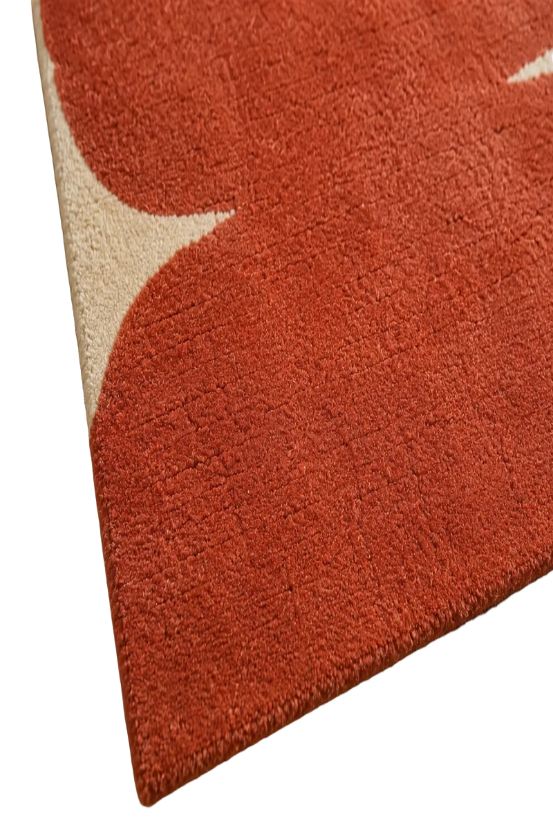 A close-up of a plush area rug with a terracotta red and cream abstract floral pattern, shown resting on a woven jute mat.